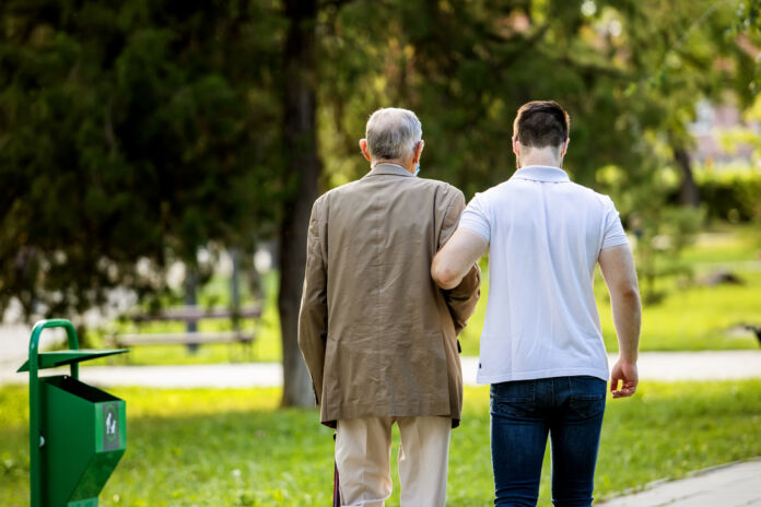 Grandfather and grandson spending quality time in park talking and walking with covid masks