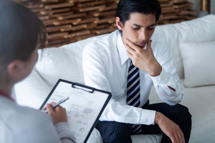 浮かない表情で精神科医に相談する男性社員 Salute e prevenzione